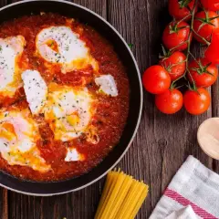 Uova al pomodoro in padella, con pomodorini freschi, basilico e un cucchiaio di legno, pronte per essere gustate.
