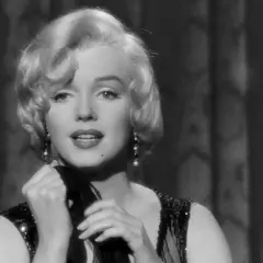 Marilyn Monroe i en ikonisk scen från en klassisk film. Hennes blonda lockar, pärlörhängen och glittriga klänning fångar blicken.