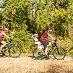 Rodzina na rowerach cieszy się aktywnym wypoczynkiem. Mama z bagażem, tata z córką w foteliku i mały chłopiec na swoim rowerze – idealny przykład turystyki rowerowej.