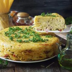 Pyszne spaghetti z piekarnika, zapiekane w formie, z kawałkami boczku i posypane natką pietruszki.