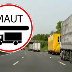 Znak MAUT informuje o opłatach drogowych w Niemczech dla pojazdów do 7,5 tony. Na autostradzie widać sznur ciężarówek.