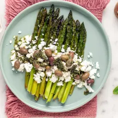 Asparagi grigliati con formaggio simile alla feta, olive e salsa verde. Un piatto fresco e saporito.