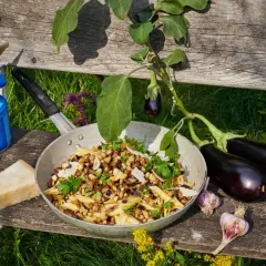 Pasta melanzane mit frischen Auberginen, Knoblauch und Parmesan. Ein Campingkocher und Zitrone deuten auf ein Outdoor-Mahl hin.