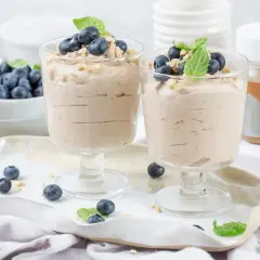 Dwa pucharki z kremowym keto deserem, udekorowane borówkami i miętą. Obok miseczka z borówkami i słoiczek Keto Cream.