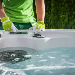 Osoba w zielonej koszulce i rękawiczkach obsługuje panel sterowania jacuzzi.