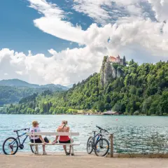 Para odpoczywa na ławce, podziwiając zamek na skale nad jeziorem Bled. Idealne miejsce na camping Bled Slovenia.