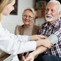 Un médecin vérifie la tension d'un homme âgé, 15/8 de tension, tandis que sa femme souriante observe.