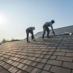 Dwóch dekarzy pracuje na dachu, układając dachówki.