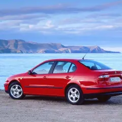 Czerwony Seat Toledo 2 na plaży, z widokiem na morze i góry w tle. Idealny na wakacyjną podróż.