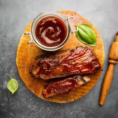 Soczyste żeberka w sosie barbecue, gotowe do podania. Obok słoiczek z sosem do steka i pędzelek.