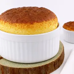 Deux soufflés au fromage dorés, prêts après leur temps de cuisson. L'un est dans un grand ramequin blanc, l'autre dans un plus petit.
