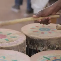 Mani che percuotono tamburi decorati con motivi solari, creando la vibrante musica africana.
