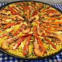 Paella mar y montaña, un festín de arroz amarillo con gambas, pimientos rojos y verduras.