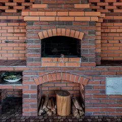 Solidny, murowany prosty grill z cegły, gotowy na letnie przyjęcia. Obok zlew i drewniana beczka.