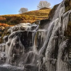 Cascada helada en los valles pasiegos, con el sol brillando sobre la ladera y el cielo azul.
