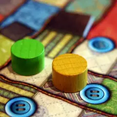 Zwei Holzfiguren auf einem bunten Brettspiel mit Knopf-Symbolen. Perfekt für die besten 2 Spieler Brettspiele.