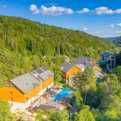 Idealne atrakcje na majówkę: kompleks hotelowy w otoczeniu zielonych lasów, z basenem i miejscami do wypoczynku.