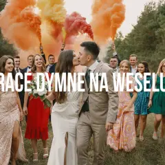 Para młoda całuje się na tle weselnych gości, którzy trzymają race dymne w kolorach tęczy.