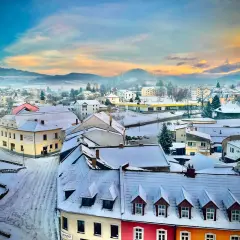 Zimowy krajobraz miasta w Czechach blisko granicy. Śnieg pokrywa dachy i ulice, a w oddali widać wzgórza.