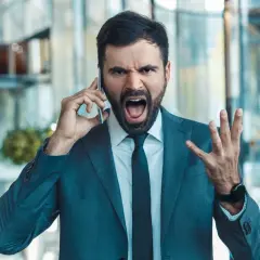 Mężczyzna w garniturze krzyczy do telefonu, pokazując, jak reagować gdy szef krzyczy.