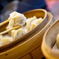 Dampfende Dumplings werden mit Stäbchen aus einem Bambuskorb gehoben. Ein köstliches Dumplings Rezept zum Nachmachen.