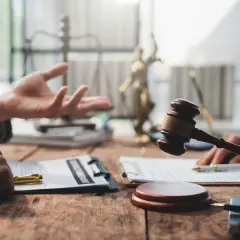 Dwie osoby przy drewnianym stole, jedna gestykuluje, druga trzyma młotek sędziowski. W tle waga sprawiedliwości i Statua Temidy. Pytanie: ile czasu ma sąd na wysłanie uzasadnienia wyroku?