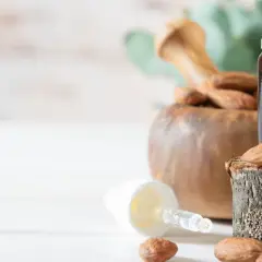 Naturalne piękno na lato: olejek migdałowy w buteleczce z pipetą, obok pestek migdałów i moździerza. Kwas migdałowy latem to sekret gładkiej skóry.