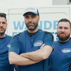 Drei Männer in blauen Arbeits-T-Shirts stehen vor einem weißen Transporter. Sie sind Teil des ATG-Teams, das sich auf Mauertrockenlegung spezialisiert hat.