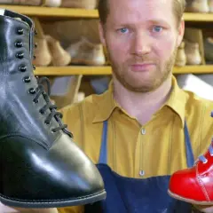 Schuhmacher hält einen schwarzen und einen roten Schuh, die für Klumpfuß-Kinder gefertigt wurden.