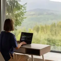 Persona trabajando en su portátil con vistas a un bosque y montañas. El estilo de vida de viajar trabajando es posible.