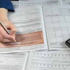 Ręka z długopisem wypełnia formularz PIT-37, obok leży kalkulator. To pomoc w rozliczeniu PIT 36.