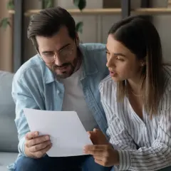 Pareja revisando un documento importante, quizás donde se firma la fein. Él la abraza mientras ambos se concentran en el papel.
