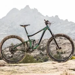 A 2020 Giant Reign mountain bike rests on a rocky outcrop, ready to conquer the rugged, misty mountains in the background.