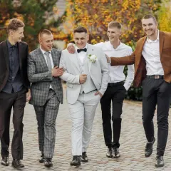 Pięciu mężczyzn w eleganckich garniturach idzie razem. Inspiracja, jak ubrać się na wesele mężczyzna.