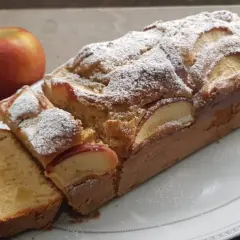 Plumcake alle mele soffice e profumato, cosparso di zucchero a velo, con fette di mela a vista. Una mela rossa intera sullo sfondo.