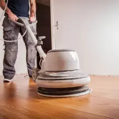 Un ouvrier utilise une ponceuse pour appliquer de l'huile sur un parquet en bois.