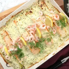Lax med apelsinsås, toppad med räkor och citronklyftor, serveras i en ugnsform. Dillkvistar ger en fräsch touch.