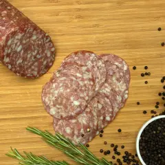 Kawałek salami napoli i kilka plastrów na desce z rozmarynem, pieprzem i solą.