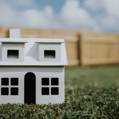 Biały model domu na trawie, z drewnianym płotem w tle. Symbolizuje marzenie o własnym domu, nawet przy minimalnej powierzchni działki budowlanej.