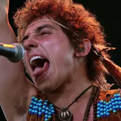 Josh Kiszka z Greta Van Fleet, jeden z członków zespołu, śpiewa z pasją do mikrofonu, ozdobiony piórami i koralikami.