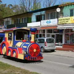 Kolorowy pociąg turystyczny w Krynicy Morskiej, gotowy do podróży po nadmorskiej promenadzie.