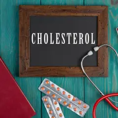 Lekarz bada cholesterol. Na drewnianym tle leżą stetoskop, książka, tabletki i opakowania leków, w tym Lipanthyl.