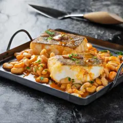 Dos lomos de bacalao a la llauna, dorados y jugosos, reposan sobre una cama de alubias blancas en salsa.
