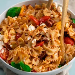 Farfalle-Nudelsalat mit frischen Tomaten, Mozzarella und sonnengetrockneten Tomaten, garniert mit Basilikum.