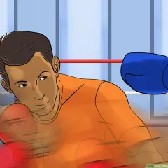 Boxer in orange shirt dodges a blue-gloved punch with a bob and weave motion in a boxing ring.