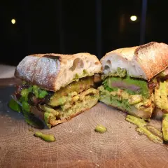 En saftig steak sandwich med avokado och en grön sås, upplagd på en träskärbräda.
