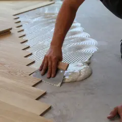 Mano stende colla per parquet incollato. Listelli di legno pronti per essere posati.