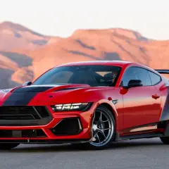 Czerwony mustang shelby z czarnymi pasami i spojlerem na tle pustynnych gór.