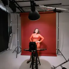 Modelka w studiu, testująca różne rodzaje oświetlenia w fotografii. Czerwone tło, lampy studyjne i sprzęt do tworzenia efektów.
