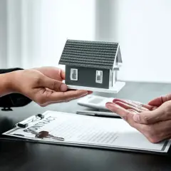 Manos entregan maqueta de casa sobre contrato. Posible exención IRPF venta vivienda heredada.